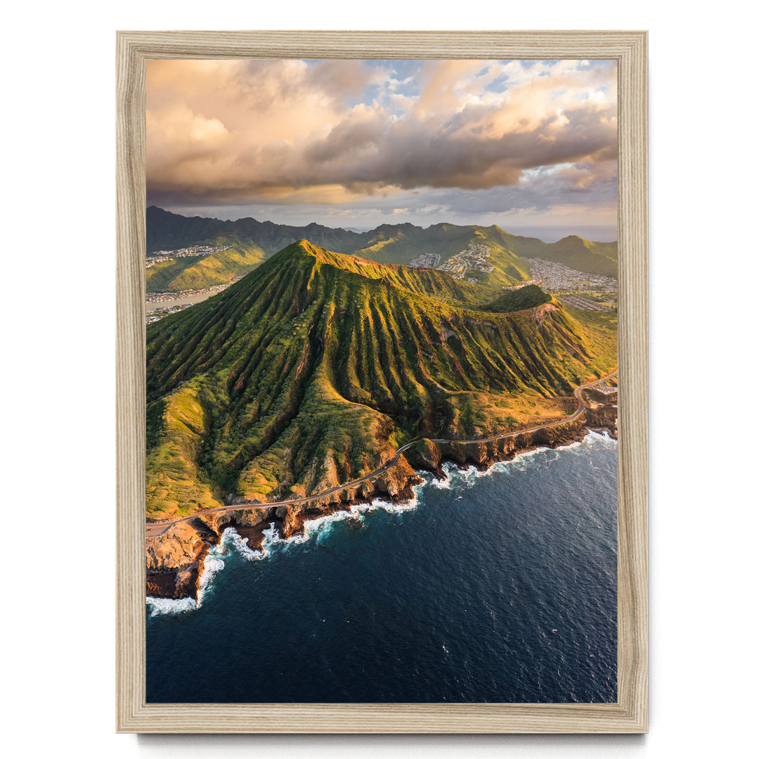 a stunning mountainous landscape with a winding road cutting through the rugged terrain. The mountains are covered in lush greenery, and the sky above is filled with clouds, creating a dramatic backdrop. The ocean is visible in the foreground, adding to the picturesque scene.
