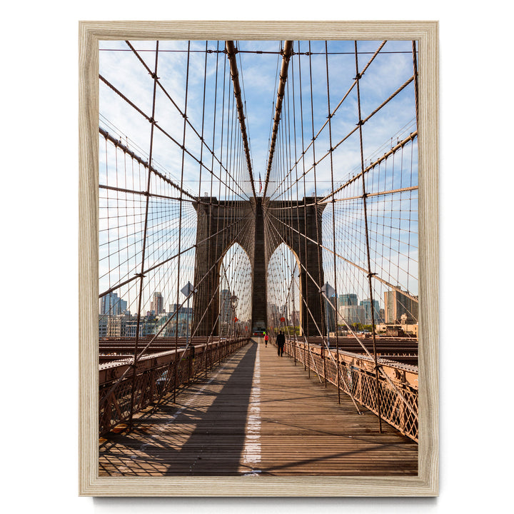 the iconic Brooklyn Bridge, with its distinctive arches and suspension cables, spanning across the frame. The bridge is surrounded by a cityscape, with tall buildings visible in the background. A person can be seen walking on the bridge, adding a sense of scale and human presence to the scene.