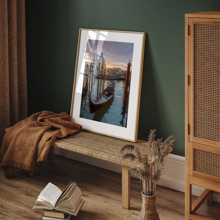 a framed photograph of a gondola on a canal, placed on a wooden bench in a room with a green wall.