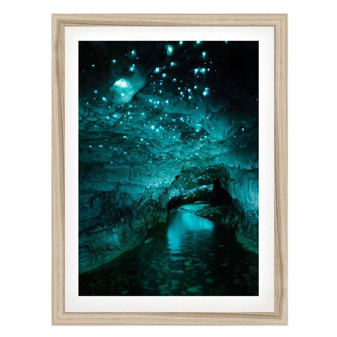 A framed photograph depicting a cave with a stream of water flowing through it, surrounded by glowing blue and green lights that create a mesmerizing, otherworldly atmosphere.