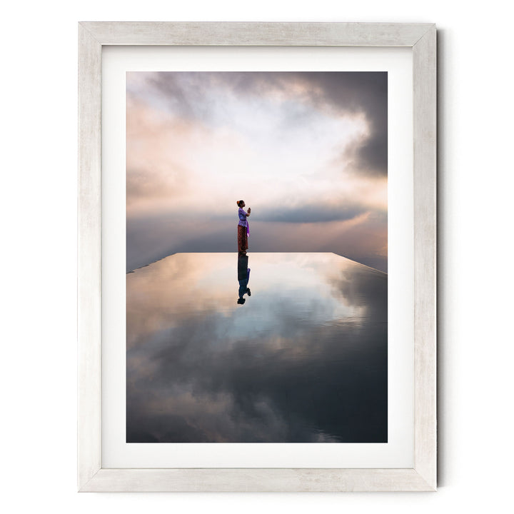 A person stands alone on a reflective surface, gazing out at the cloudy sky.