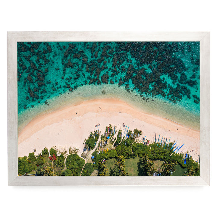 The image is an aerial view of a tropical beach with crystal clear turquoise waters, sandy shores, and lush vegetation surrounding the area.