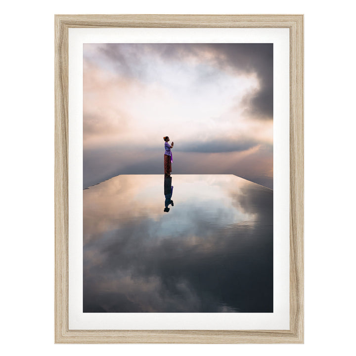 A person stands on a reflective surface, gazing out at the horizon, with a cloudy sky and a serene atmosphere in the background.