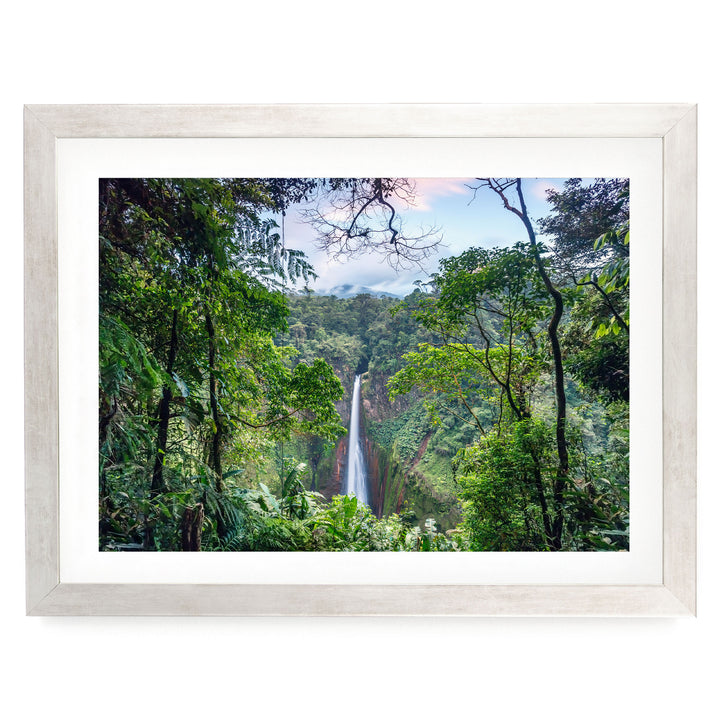 A lush, green forest with a waterfall cascading down a steep cliff, framed in a white wooden frame.