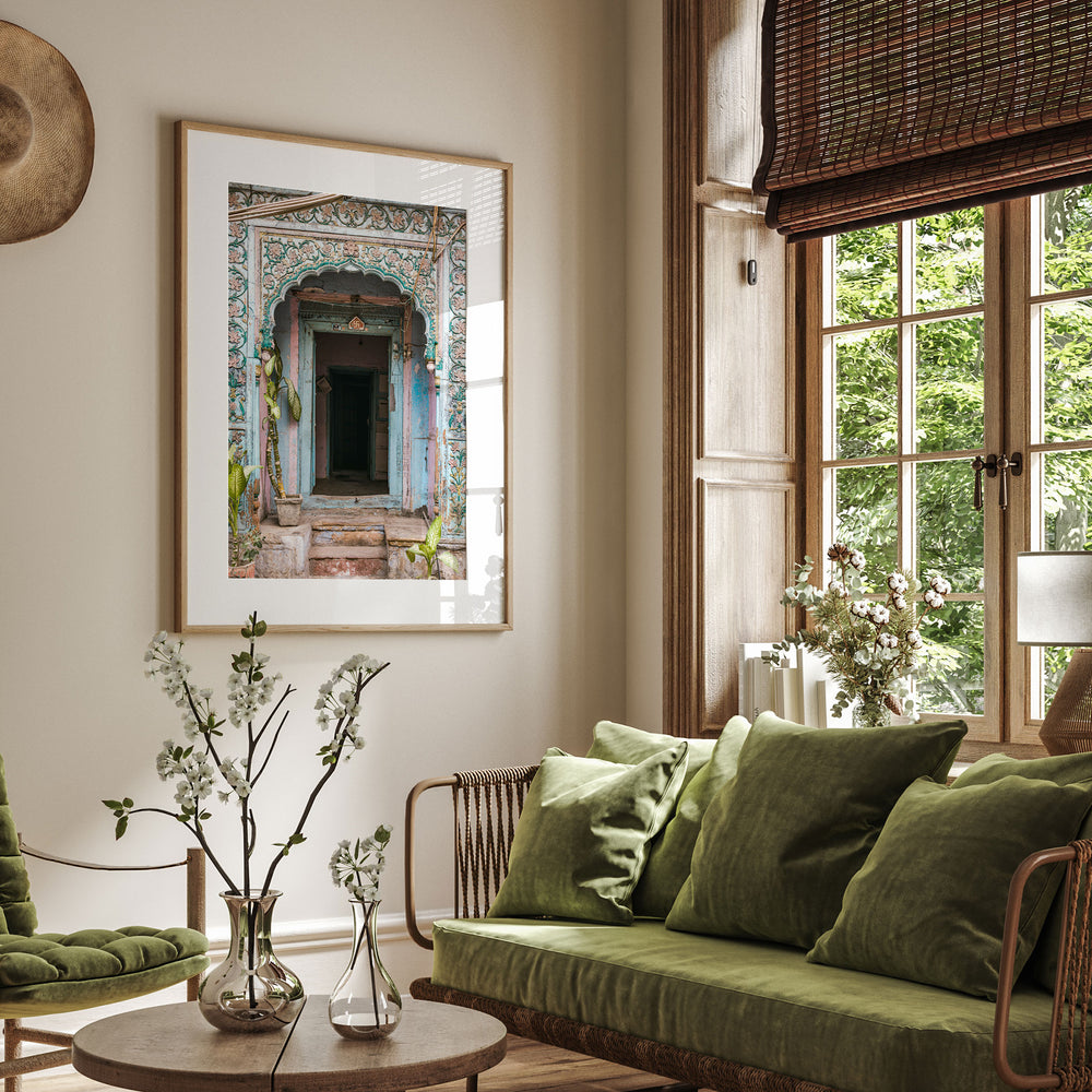 a cozy living room with a large window overlooking a lush green outdoor scene. The room is adorned with a green sofa, a wooden coffee table, and a framed picture of a colorful doorway. The room is further decorated with potted plants and vases, creating a serene and inviting atmosphere.