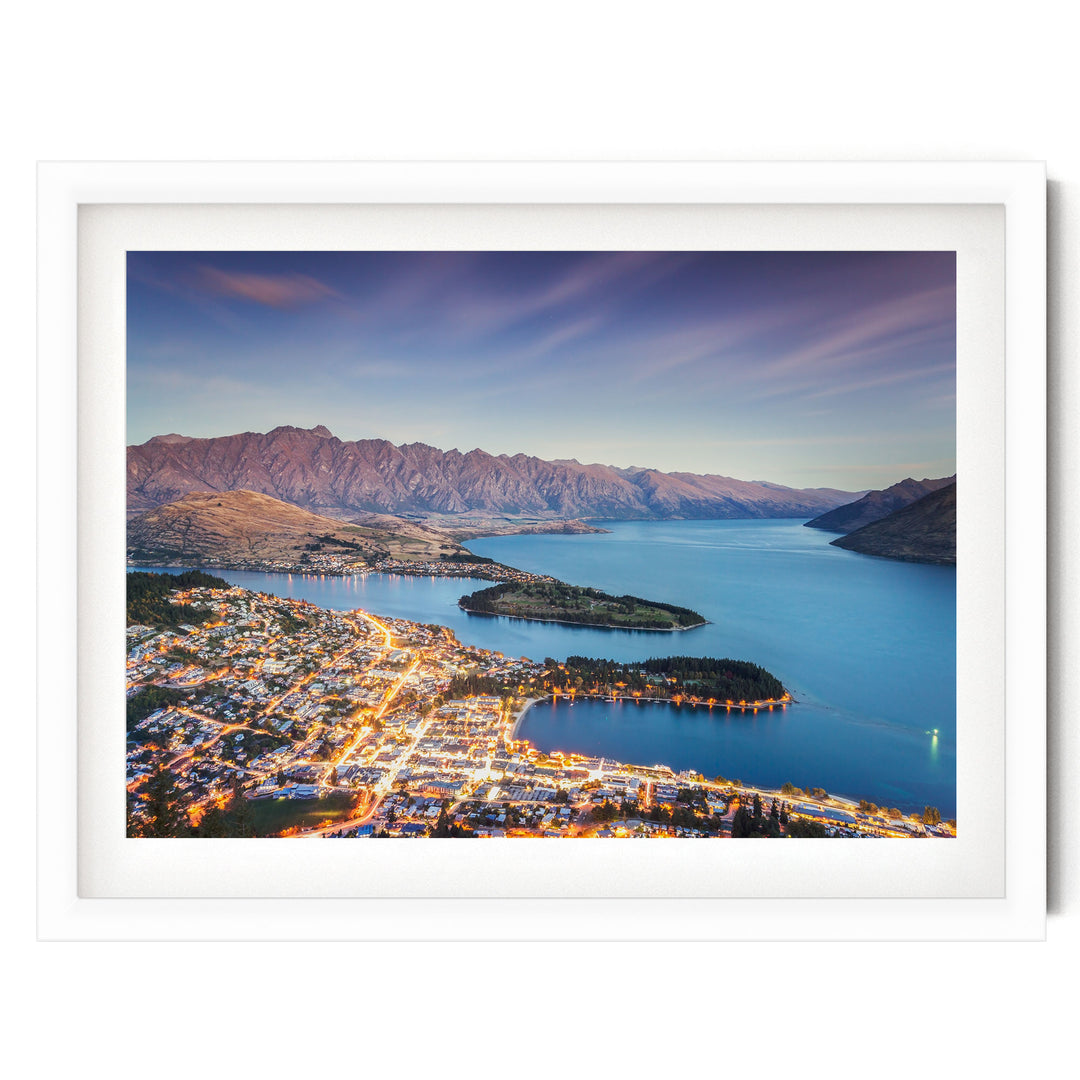 a picturesque town nestled at the foot of a mountain range, with the town's lights twinkling in the evening and the surrounding mountains bathed in a warm, golden glow.
