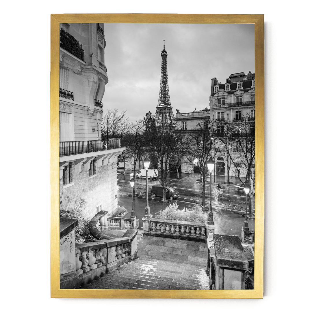 The image is a black and white photograph of the Eiffel Tower in Paris, France, with a street scene in the foreground featuring ornate buildings and lampposts.
