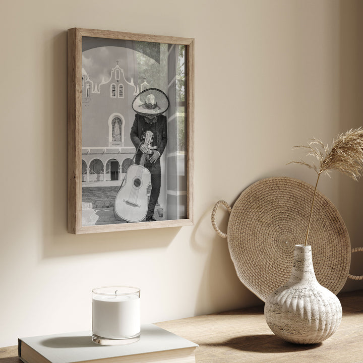 a framed black and white photograph of a person playing a guitar, hanging on a wall next to a woven basket and a candle.