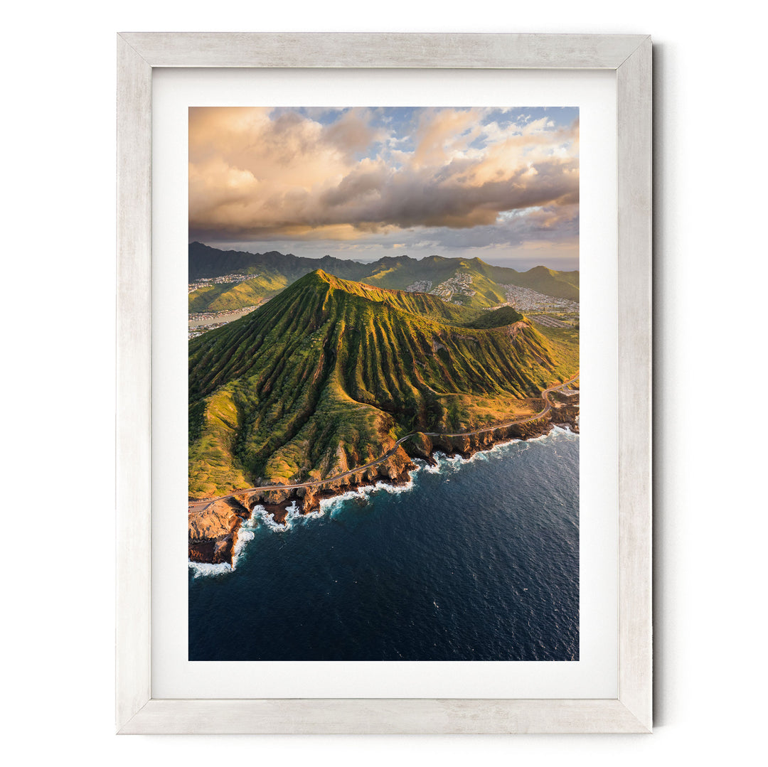 a stunning mountainous landscape with a deep blue ocean in the foreground. The mountains are covered in lush green vegetation, and the sky is filled with clouds, creating a dramatic backdrop. The ocean is dotted with small waves, adding a sense of movement to the scene. The image is framed in a white border, giving it a clean and elegant appearance.