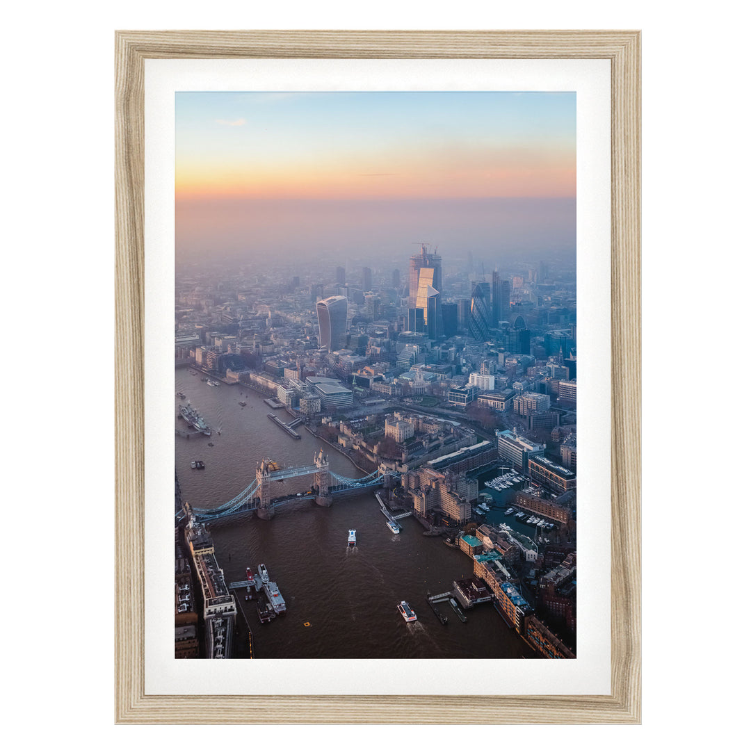 The image is an aerial view of a cityscape with a river running through it, featuring a bridge and several boats. The city is densely populated with tall buildings, and the sky is filled with warm, hazy colors, suggesting a sunrise or sunset.