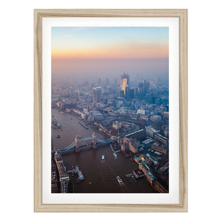 The image is an aerial view of a cityscape with a river running through it, featuring a bridge and several boats. The city is densely populated with tall buildings, and the sky is filled with warm, hazy colors, suggesting a sunrise or sunset.