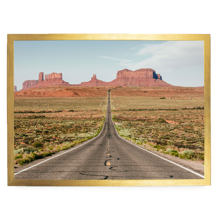 A long, straight road stretches out into the distance, leading towards a series of red rock formations in the background.