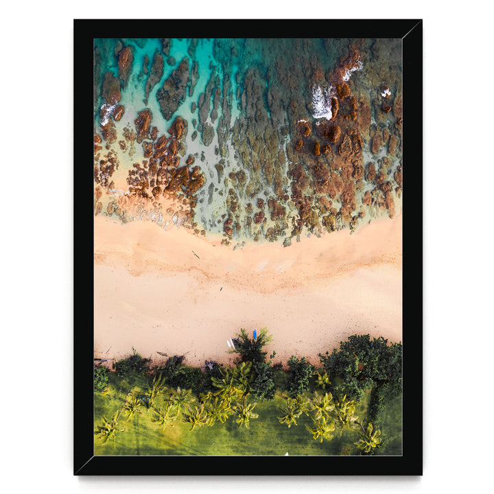 The image is an aerial view of a beach with a mix of rocky and sandy terrain, surrounded by lush greenery and palm trees.