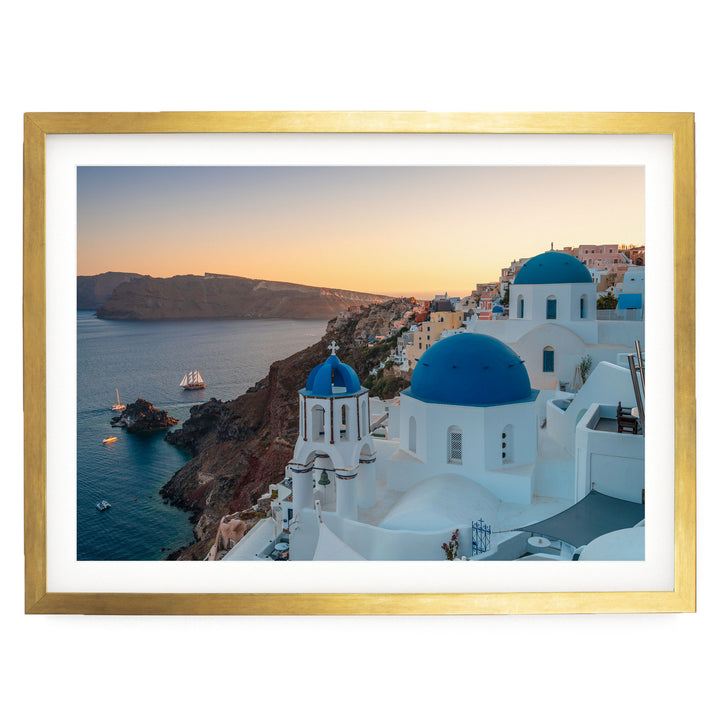 a picturesque coastal town with white buildings and blue domes, overlooking the ocean. The town is situated on a cliff, with a clear blue sky and a warm sunset in the background.