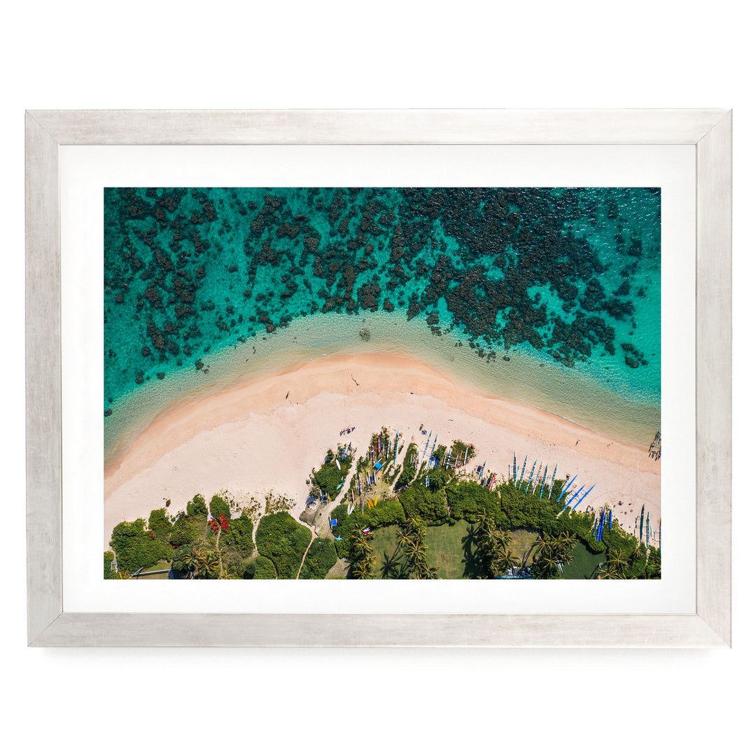 The image is an aerial view of a tropical beach with crystal clear turquoise waters, sandy shores, and lush vegetation surrounding the area.