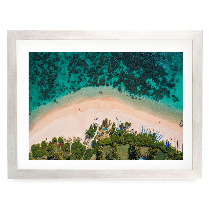 The image is an aerial view of a tropical beach with crystal clear turquoise waters, sandy shores, and lush vegetation surrounding the area.