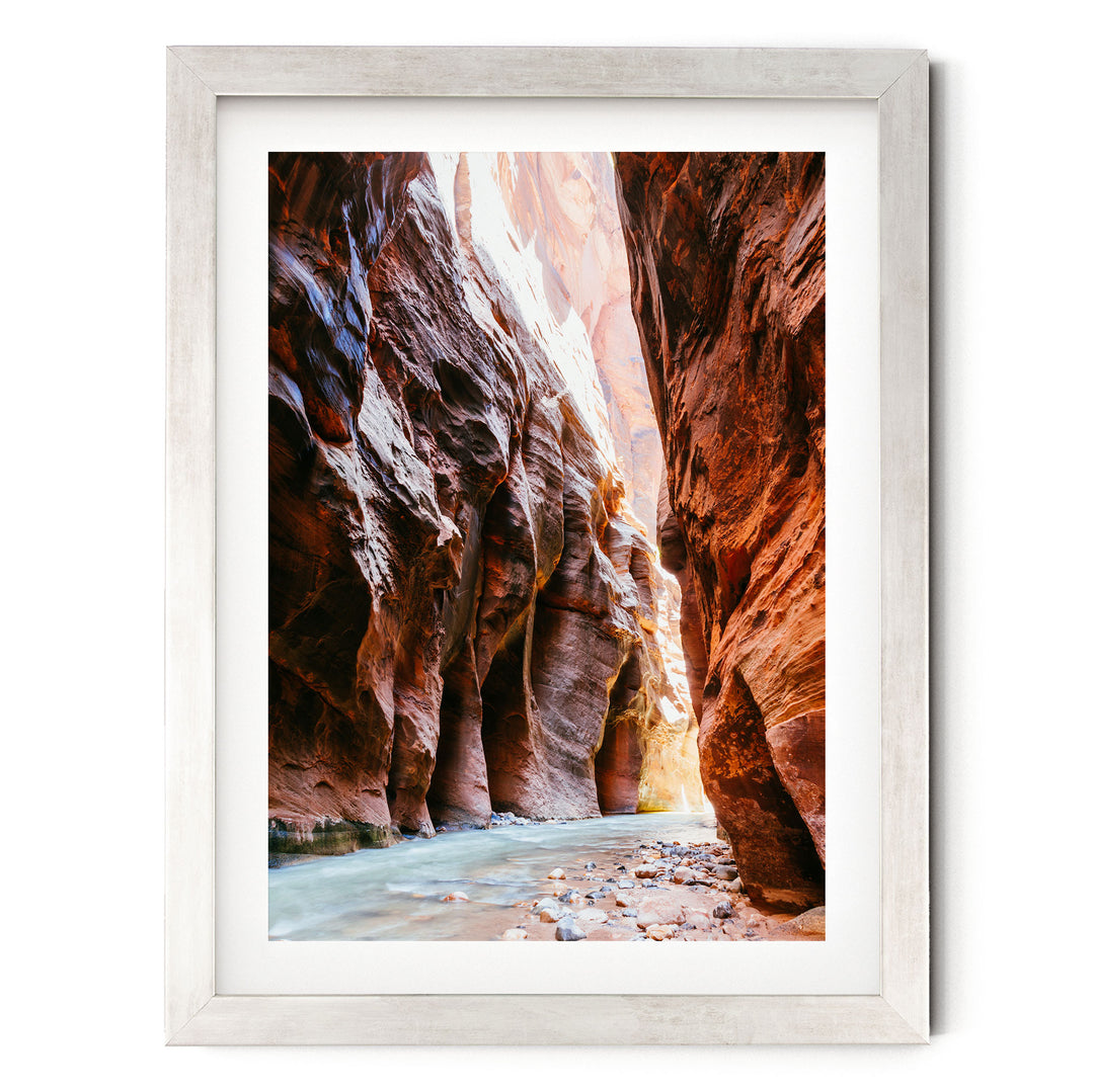 A framed photograph depicting a narrow, winding river flowing through a canyon with towering red rock walls on either side.