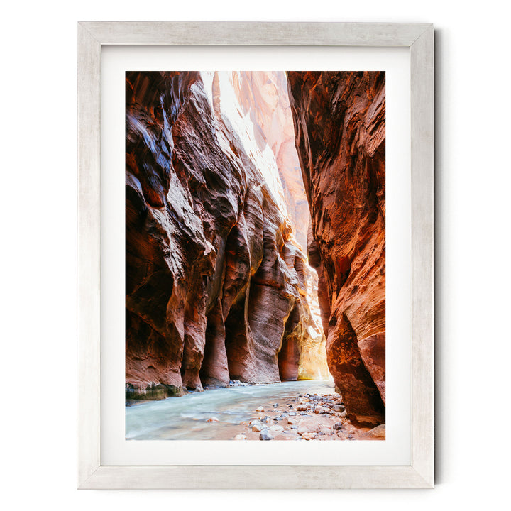 A framed photograph depicting a narrow, winding river flowing through a canyon with towering red rock walls on either side.