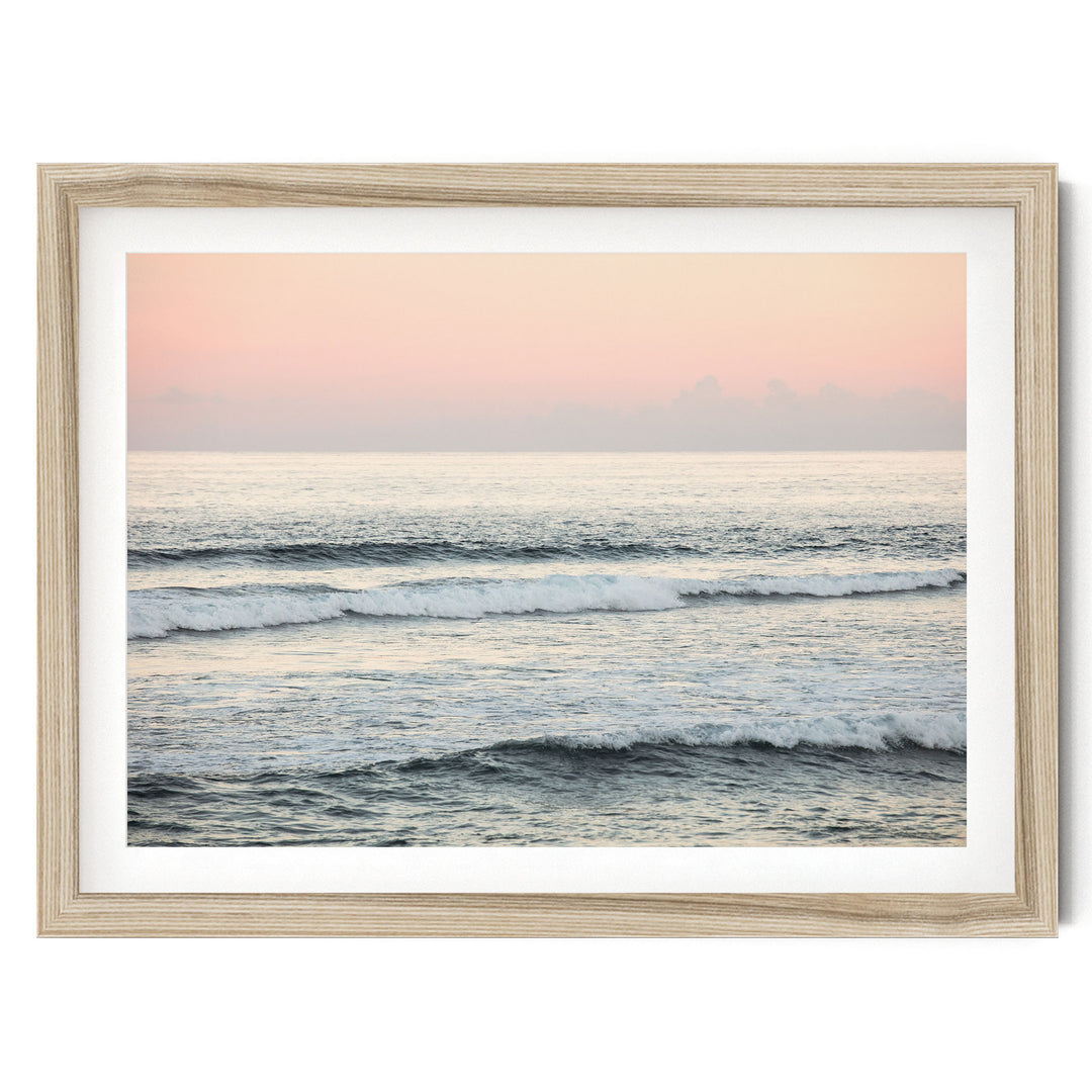 A serene ocean scene with waves gently lapping against the shore, set against a soft pink and orange sky.