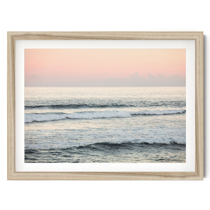 A serene ocean scene with waves gently lapping against the shore, set against a soft pink and orange sky.