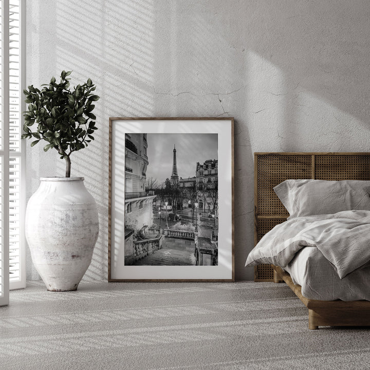 a bedroom with a large white vase, a framed black and white photograph of a cityscape, and a wooden headboard.