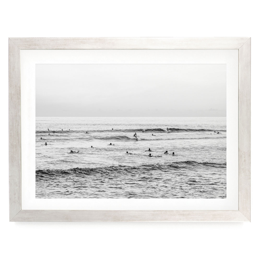 A black and white photograph of a group of people swimming in the ocean, with waves visible in the background.