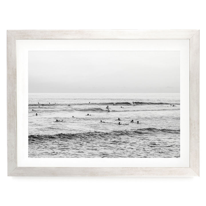 A black and white photograph of a group of people swimming in the ocean, with waves visible in the background.