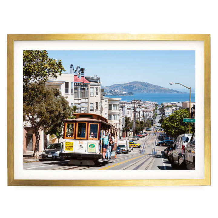 A cable car is traveling down a busy street in San Francisco, with buildings, cars, and pedestrians visible in the background.