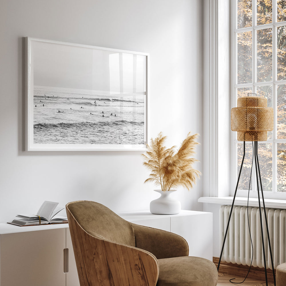 a serene and modern living room with a large framed black and white photograph of a beach scene hanging on the wall, a wooden chair, a white side table, and a floor lamp with a beige lampshade.