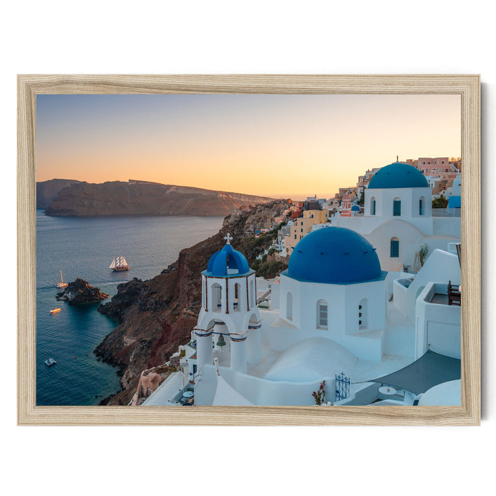 a picturesque coastal town with white buildings and blue domes, overlooking the ocean. The town is situated on a cliff, with a rocky shoreline and a small boat visible in the water. The sky is painted in warm hues of orange, indicating the setting sun. The overall scene is serene and idyllic, showcasing the beauty of the Greek island.
