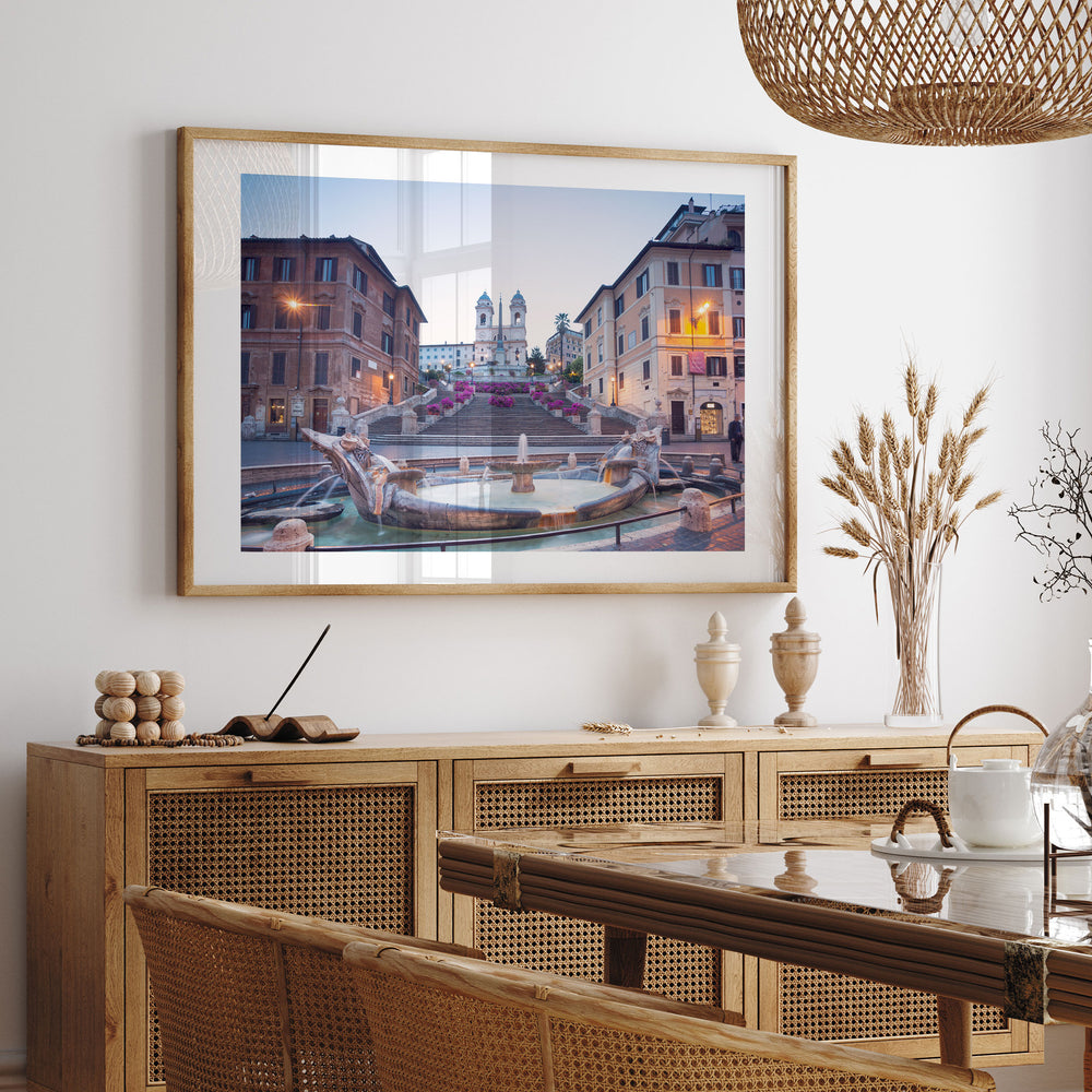 a framed photograph of the St. Peter's Square in Rome, Italy, hanging on a wall above a wooden cabinet.