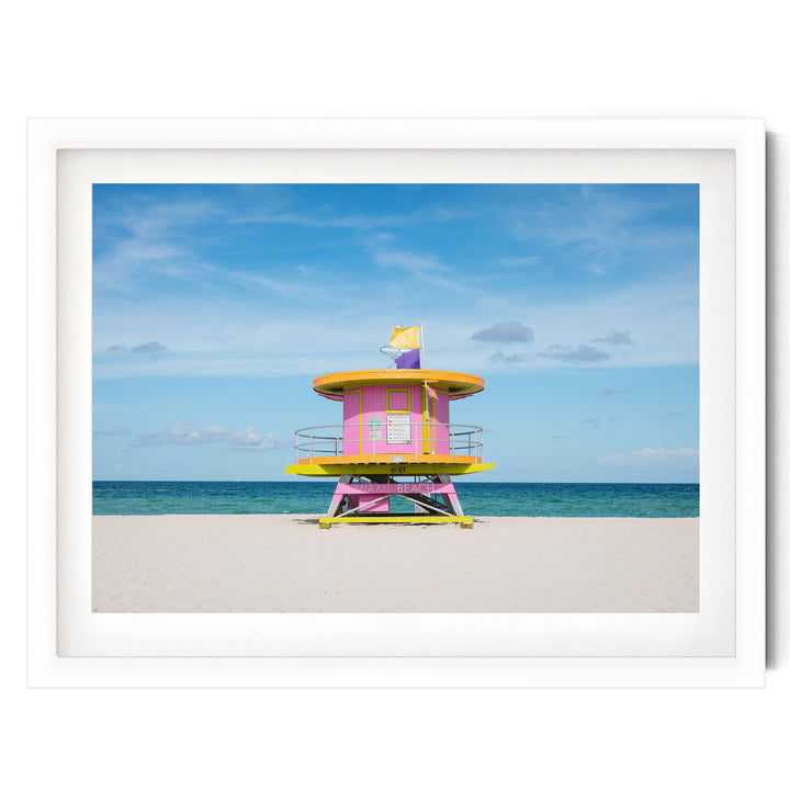 A lifeguard tower painted in pink and yellow stands on a sandy beach, with the ocean visible in the background.