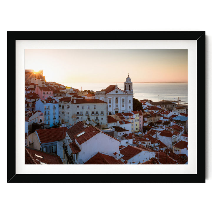 A picturesque view of a coastal town with colorful buildings, a church with a bell tower, and the sun setting over the ocean in the distance.