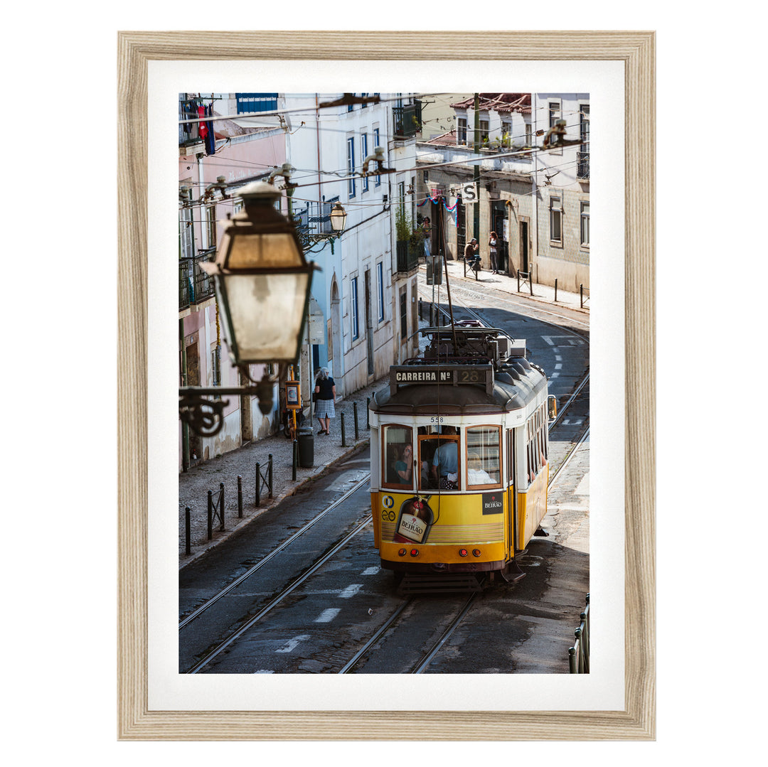 A yellow tram is traveling down a street lined with buildings and lampposts.