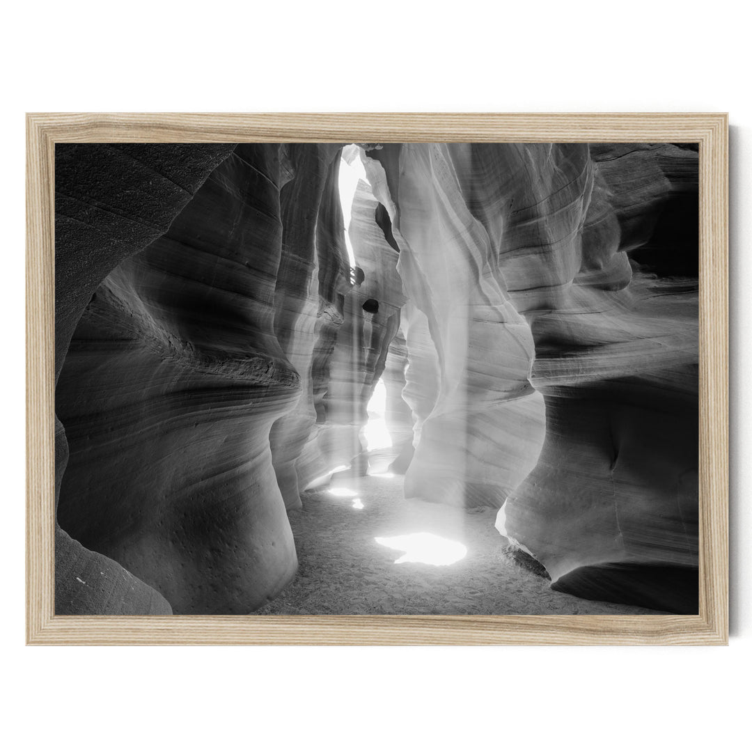 A black and white photograph of a narrow, winding path leading through a natural rock formation, with sunlight streaming through the opening and casting shadows on the walls.