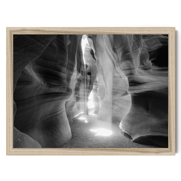 A black and white photograph of a narrow, winding path leading through a natural rock formation, with sunlight streaming through the opening and casting shadows on the walls.