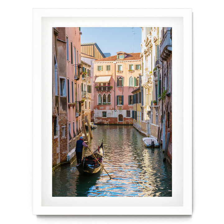 A gondolier navigates a traditional Venetian gondola through a picturesque canal, surrounded by colorful buildings and reflecting the clear blue sky.
