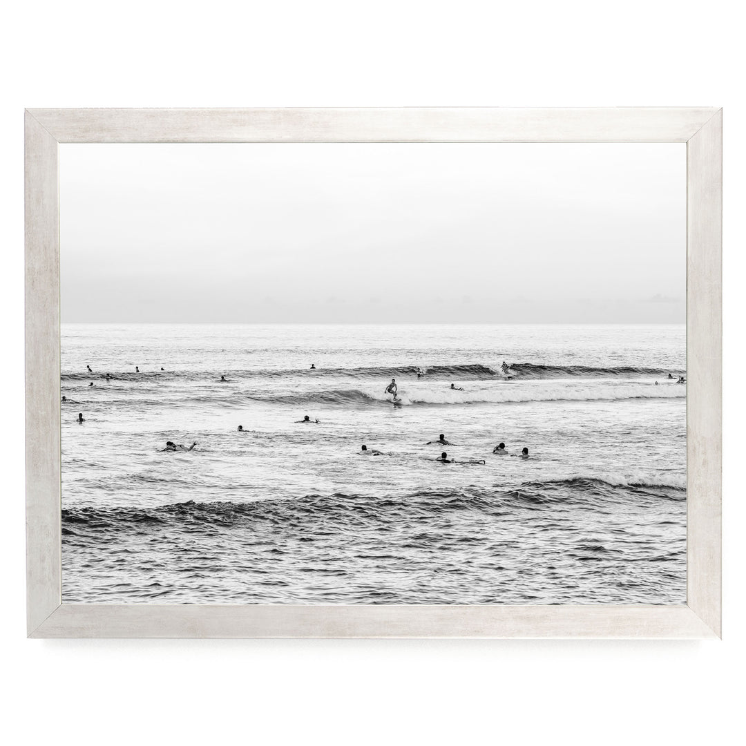A black and white image of a group of people swimming and surfing in the ocean, with waves visible in the background.
