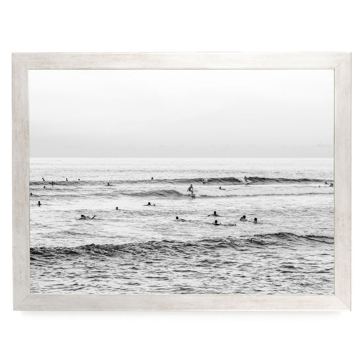 A black and white image of a group of people swimming and surfing in the ocean, with waves visible in the background.
