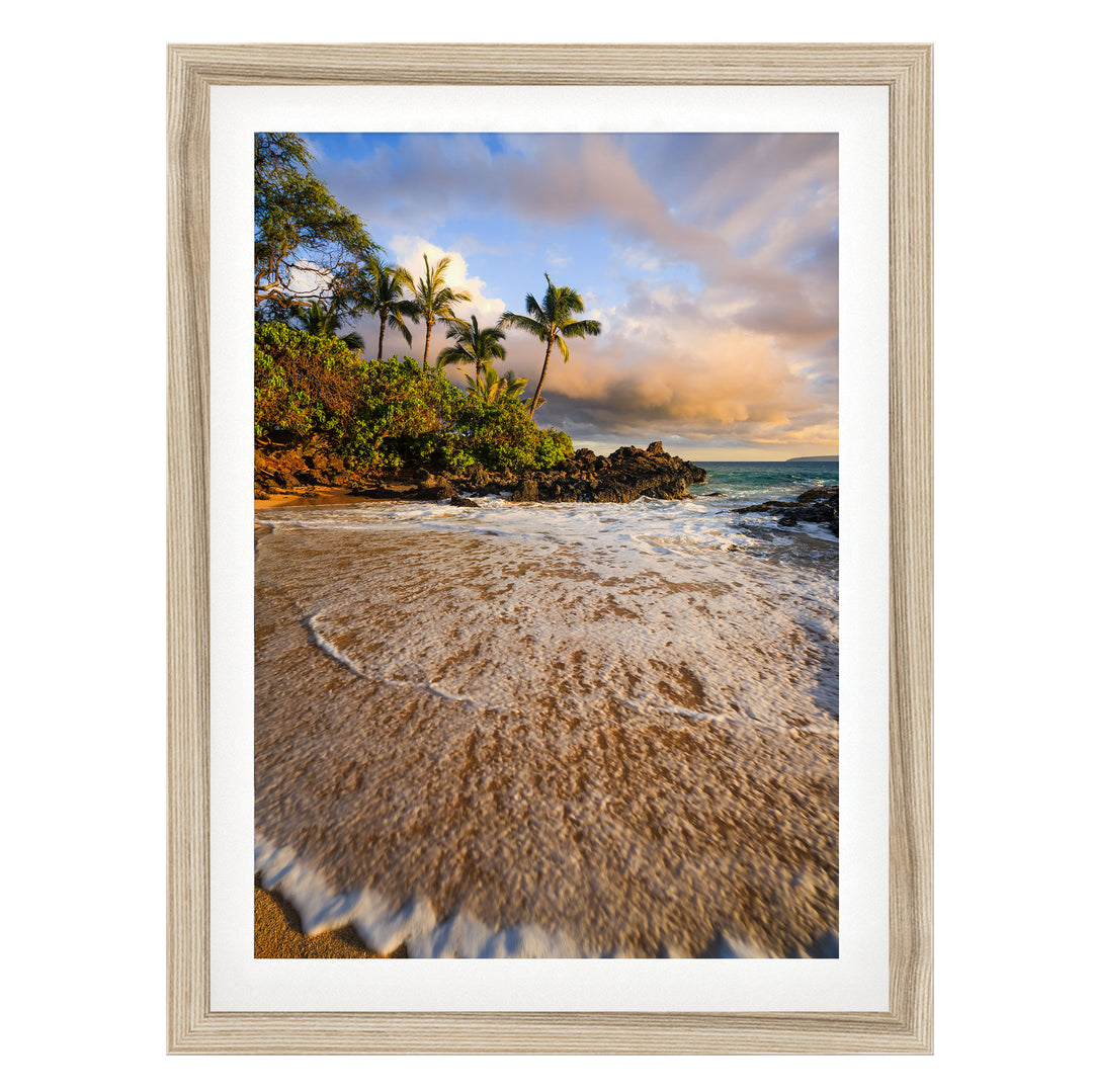 A framed photograph depicting a serene beach scene with palm trees, crashing waves, and a colorful sky at sunset.