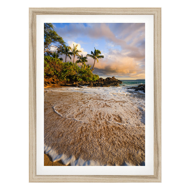 A framed photograph depicting a serene beach scene with palm trees, crashing waves, and a colorful sky at sunset.