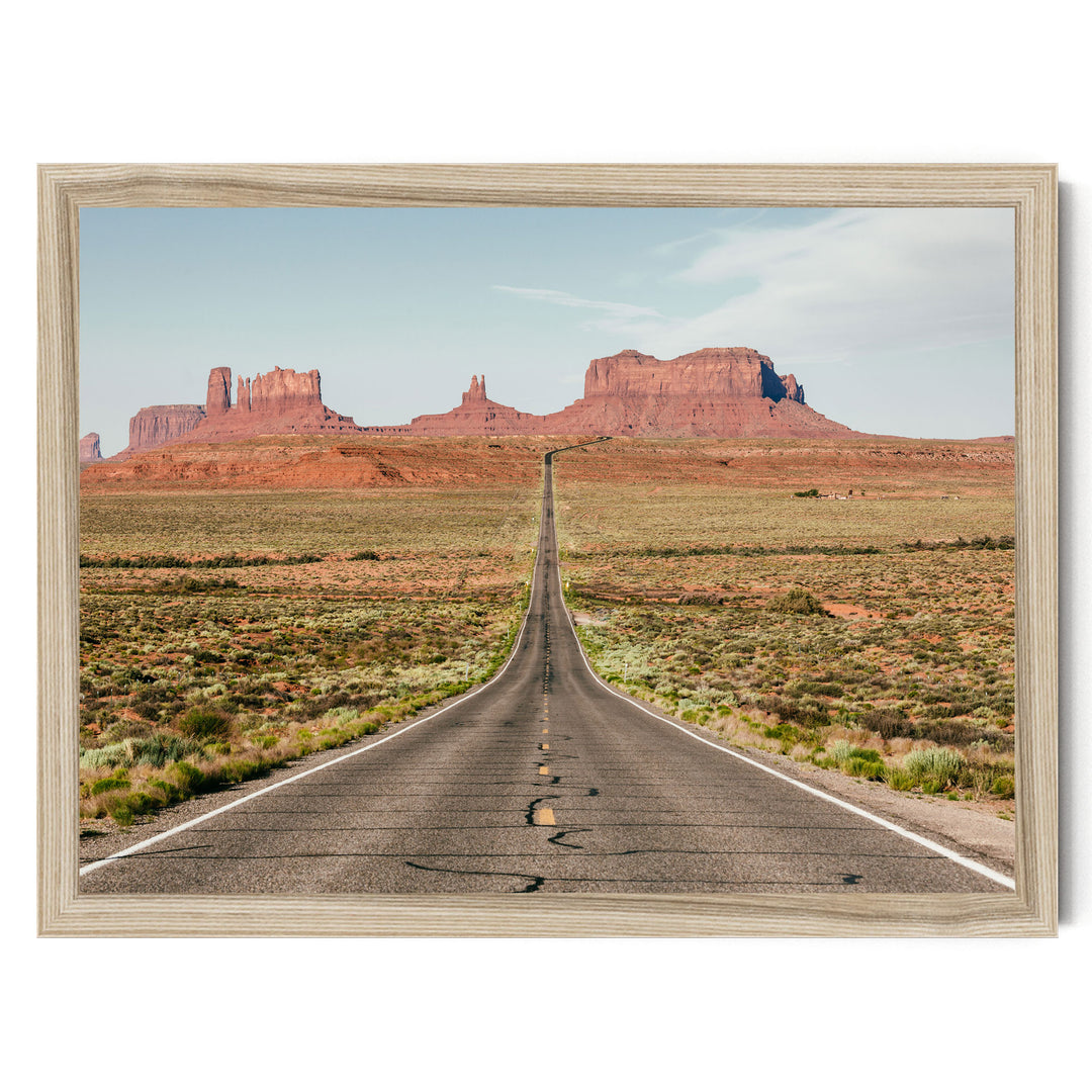 A long, straight road stretches out into the distance, leading towards a series of red rock formations in the background.