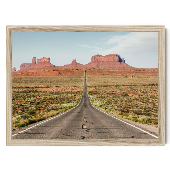 A long, straight road stretches out into the distance, leading towards a series of red rock formations in the background.