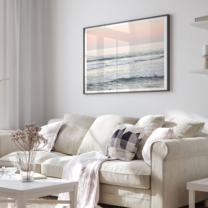 a cozy living room with a beige sofa adorned with patterned pillows, a white coffee table, and a framed picture of a serene ocean scene hanging on the wall.