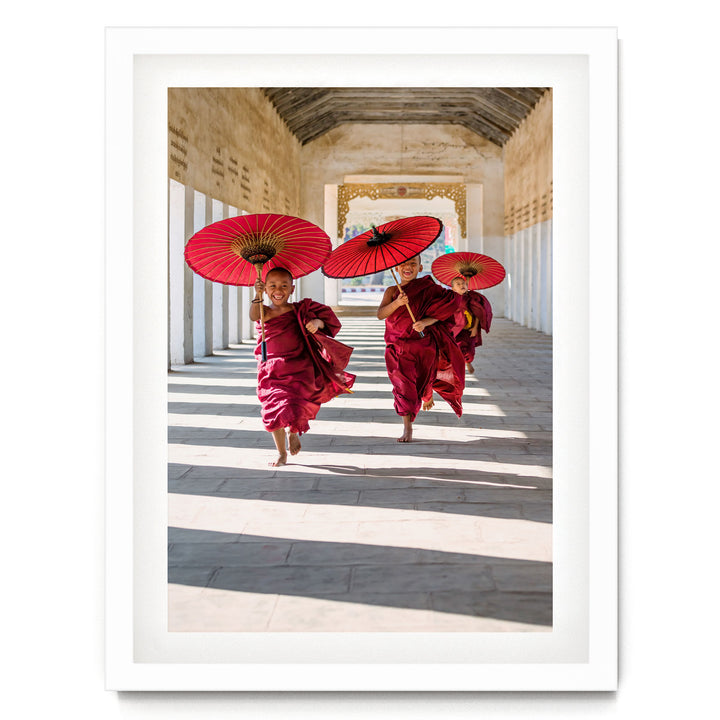 Two young monks in red robes are walking down a hallway, each holding a red umbrella.