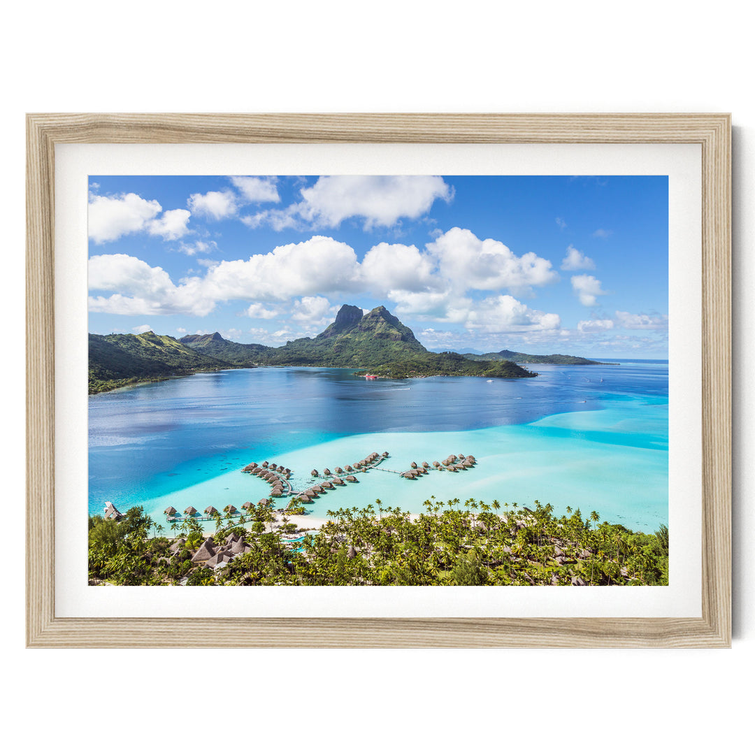 a tropical island with a clear blue sky, lush green mountains, and a turquoise ocean with several small islands and resorts in the distance.