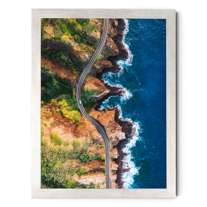The image is an aerial view of a winding road cutting through a rugged coastline with cliffs and the ocean.