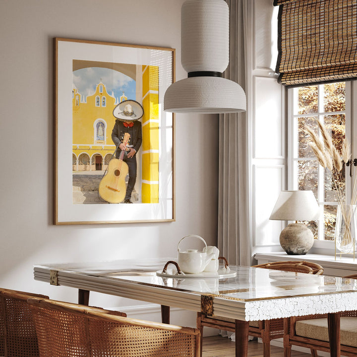 a dining room with a large framed picture of a man playing a guitar on the wall, a white table with a teapot and cups, and a window with a bamboo shade.