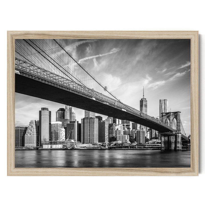 A black and white photograph of the Brooklyn Bridge spanning the East River, with the New York City skyline visible in the background.