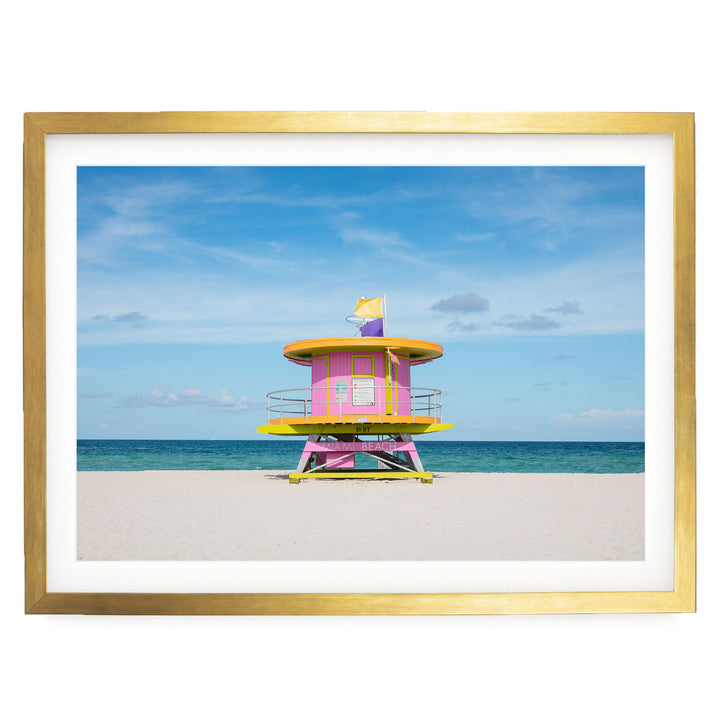 A lifeguard tower painted in pink and yellow stands on a sandy beach, with the ocean visible in the background.